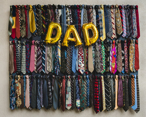 Balloons spelling 'DAD' in gold hang in front of a selection of colourful ties.
