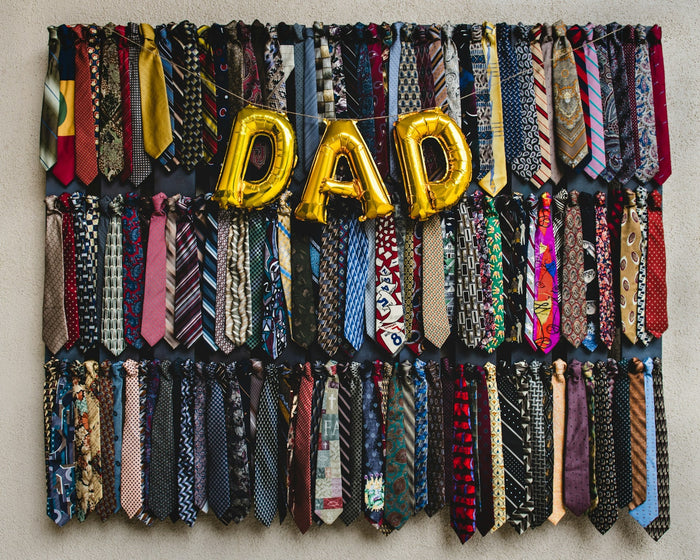Balloons spelling 'DAD' in gold hang in front of a selection of colourful ties. 
